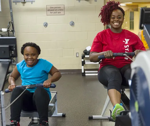 A YMCA staff person showing a young girl how to use a machine. 