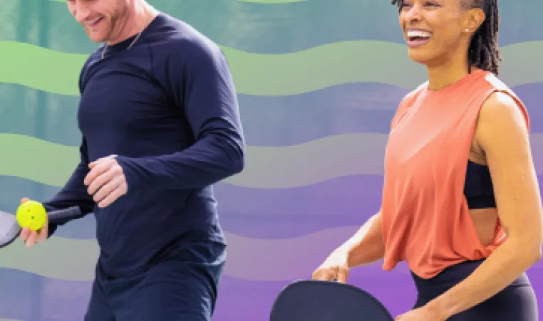 A smiling couple playing pickleball. 