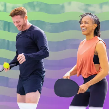 A smiling couple playing pickleball. 