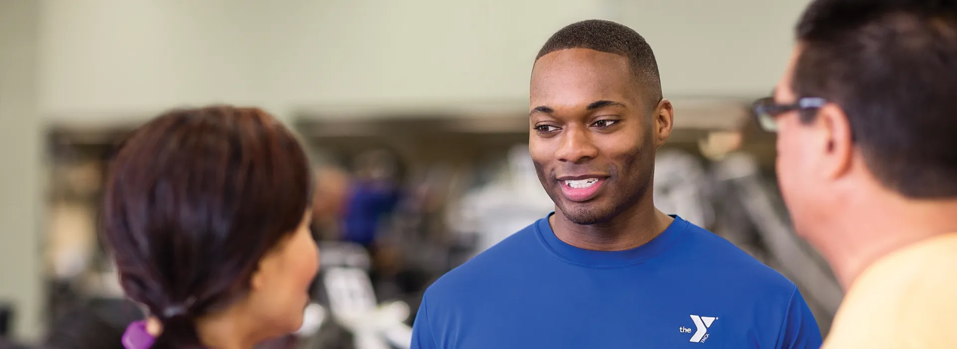 A YMCA staff member engaging in a friendly conversation with two members in the work out area.